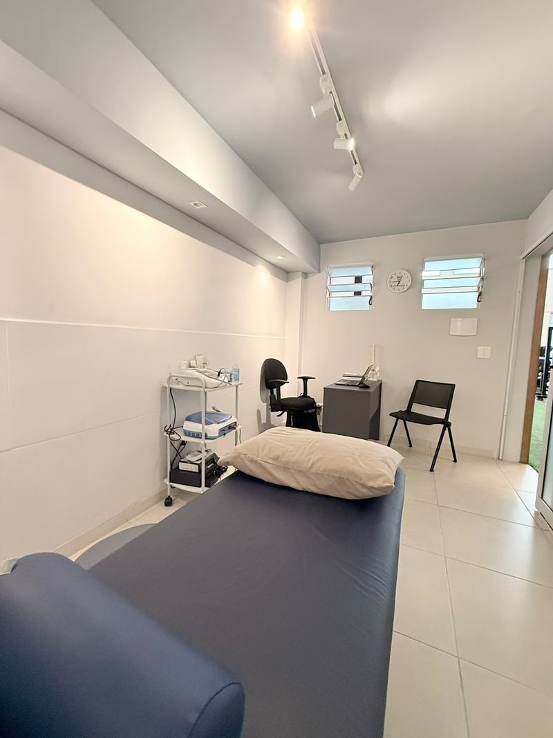 Sala de fisioterapia com maca, luz natural e equipamentos organizados